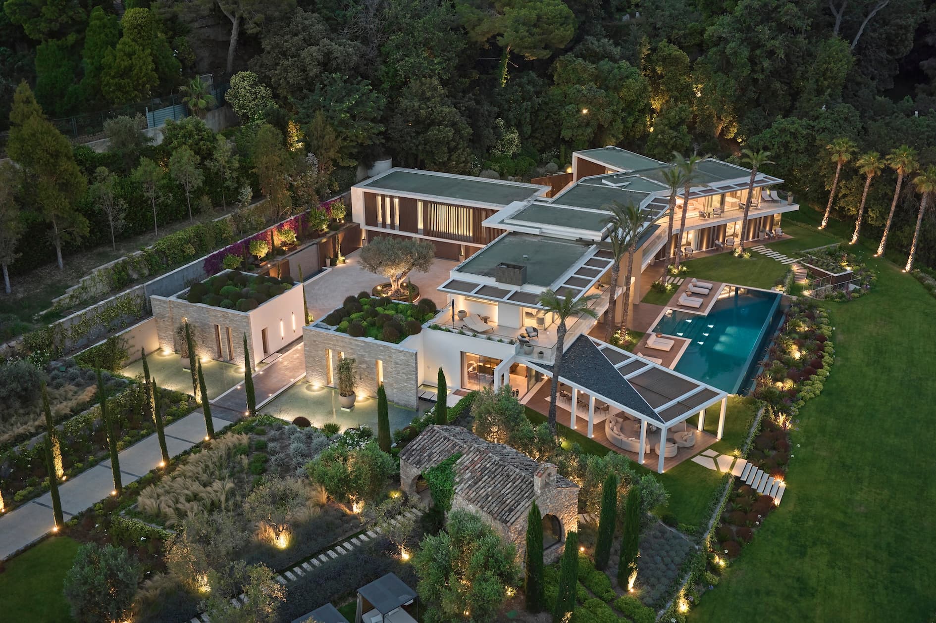 Moderne Luxusvilla in Cannes, umgeben von Garten und Pool, Außenansicht bei Nacht.