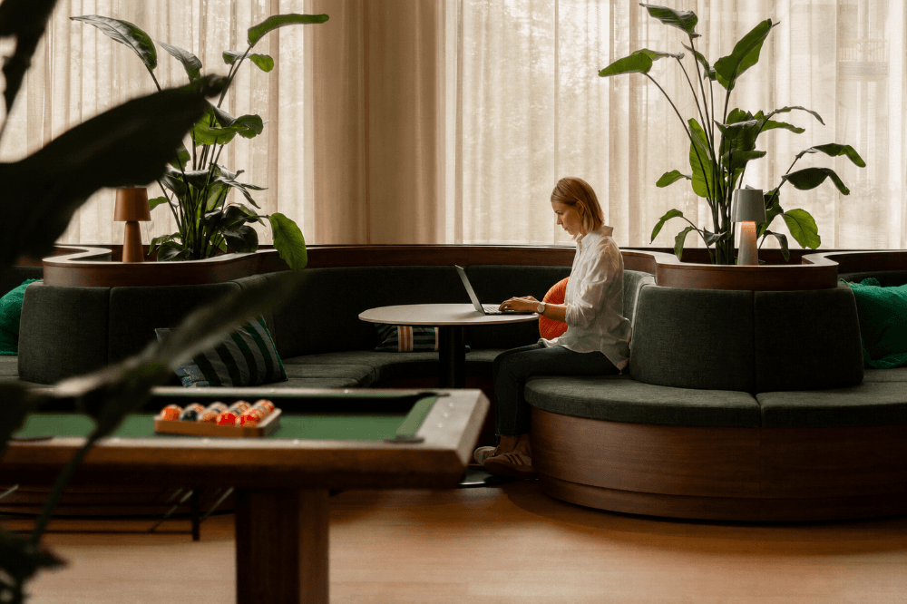 Frau arbeitet mit Laptop in modernem Lounge-Bereich mit Pflanzen im Habyt Vienna Aparthotel Wien