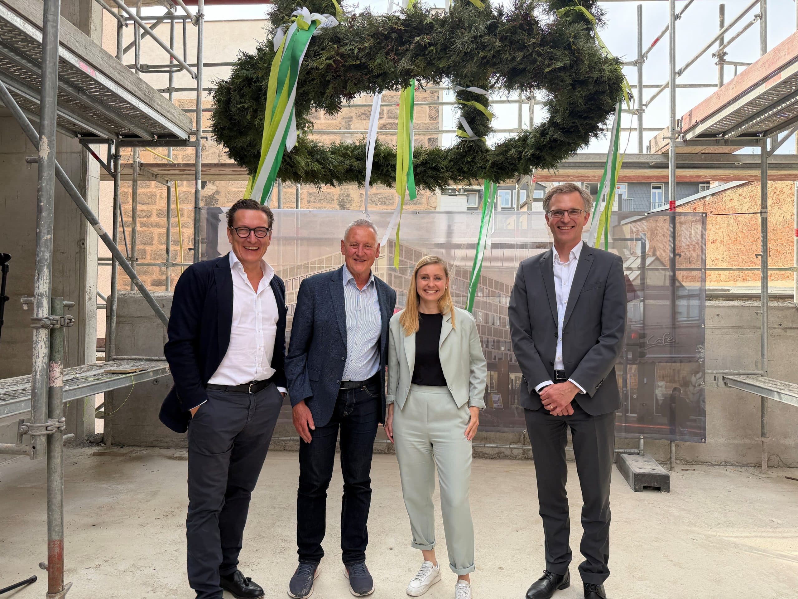 Vier Projektbeteiligte beim Richtfest des Projekts Schwabacher Straße 54 in Fürth stehen unter einer Richtkrone auf der Baustelle.
