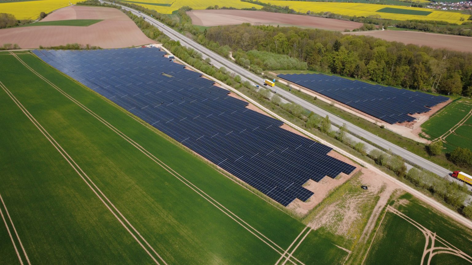 Luftaufnahme des Solarparks Bodenrode im Landkreis Eichsfeld mit Photovoltaik-Modulen neben einer Landstraße.
