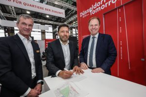 Drei Männer bei der Unterzeichnung der Eckpunktevereinbarung für das Quartier D.STRICT auf der polis Convention in Düsseldorf.