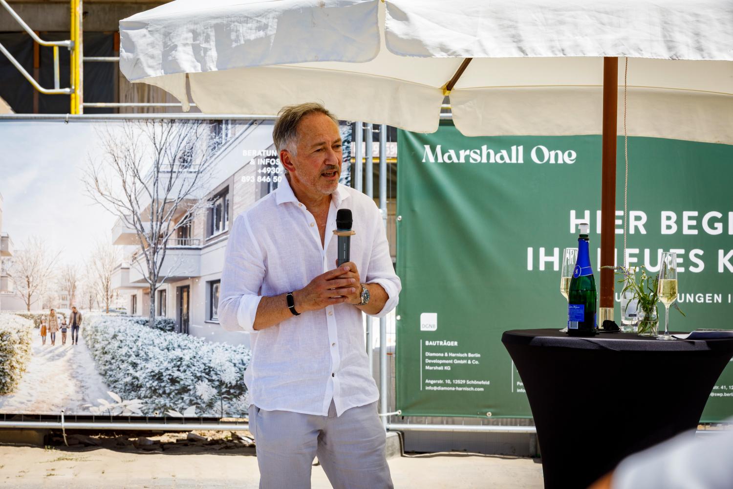 Alexander Harnisch spricht beim Richtfest von Marshall One in Berlin-Dahlem unter einem Sonnenschirm.
