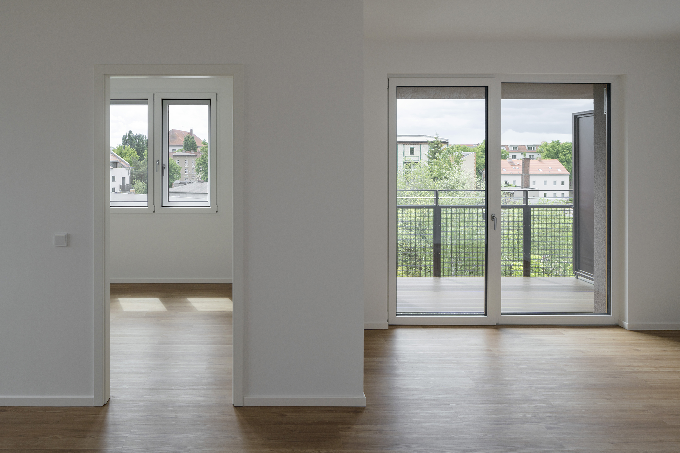 Innenraum einer neuen Wohnung der DMSW in Berlin-Pankow mit Blick durch Fenster und Balkon auf das Quartier.