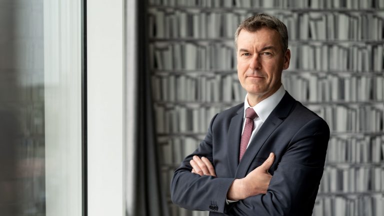Sven Mückenheim, Geschäftsführer Vertrieb bei der Dr. Peters Group steht im Anzug mit verschränkten Armen vor einem Fenster.