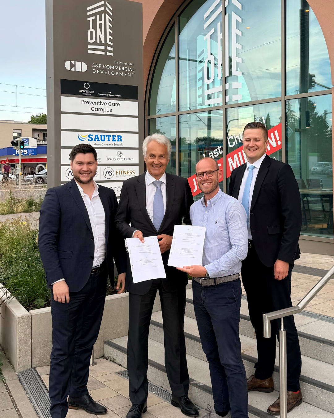 Vier Männer, darunter Vertreter von Creditreform und S&P Commercial Development, stehen vor dem Bürogebäude The One in Nürnberg und halten Verträge in den Händen.