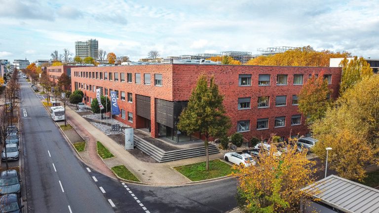 Bürogebäude an der Stockholmer Allee 32a–c in Dortmund im Herbst, rote Klinkerfassade, Straßenansicht mit Autos und Bäumen.