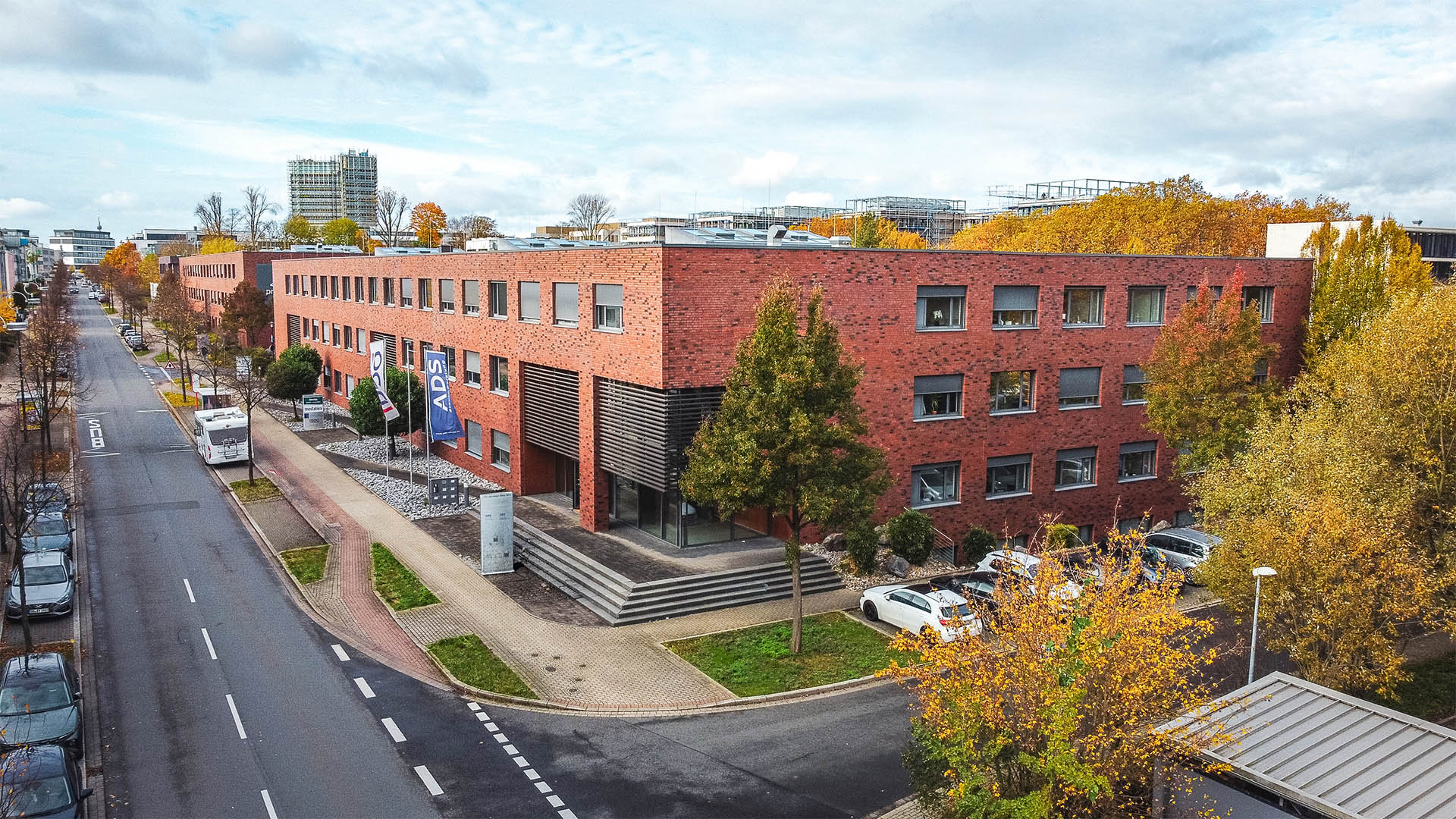 Bürogebäude an der Stockholmer Allee 32a–c in Dortmund im Herbst, rote Klinkerfassade, Straßenansicht mit Autos und Bäumen.