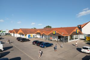 Einzelhandelsimmobilie in Halle, Außenansicht mit Parkplatz und Kunden bei sonnigem Wetter.