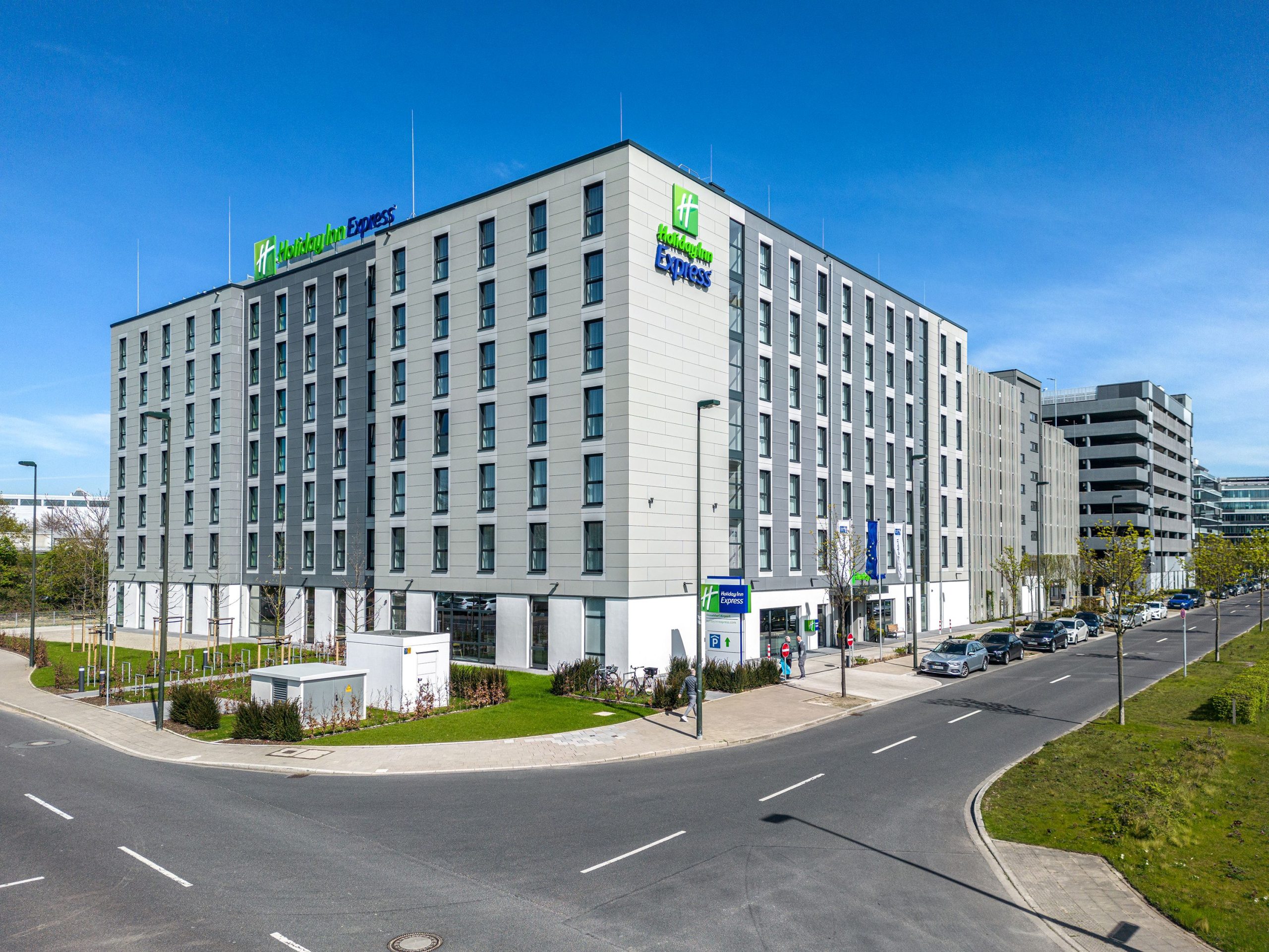 Das Holiday Inn Express Hotel in Düsseldorf nahe dem Flughafen, modernes Gebäude mit Parkhaus, Außenansicht bei Tag.